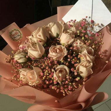Charming bouquet of pink roses and baby's breath wrapped in pink paper with a card attached.