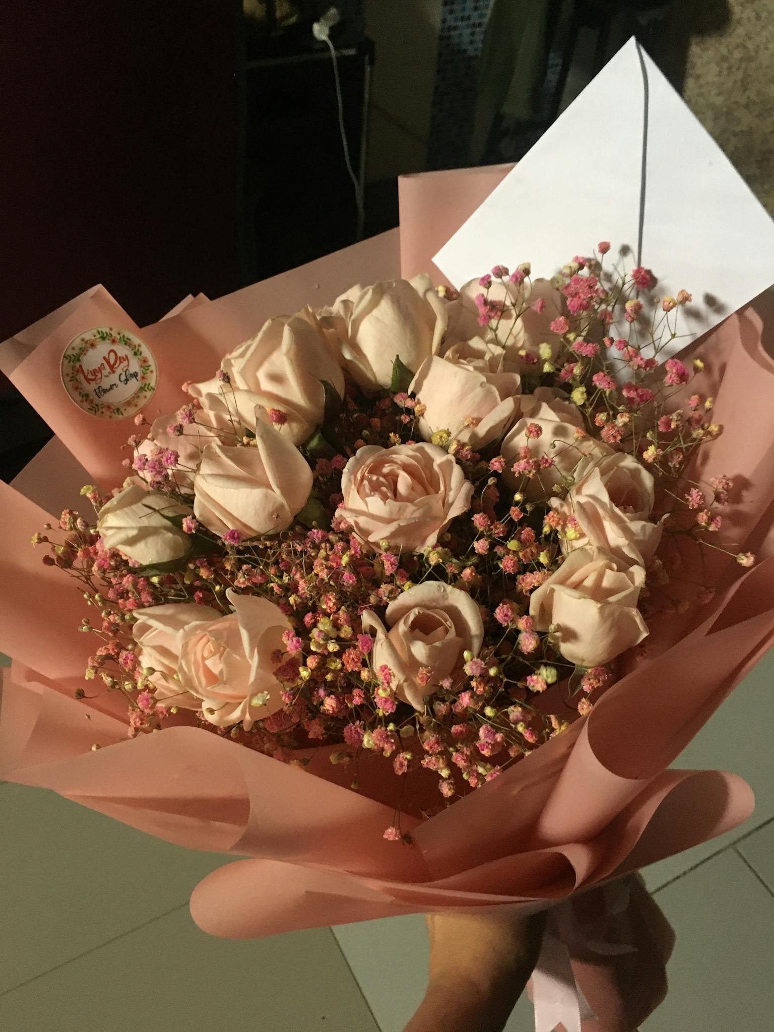 Charming bouquet of pink roses and baby's breath wrapped in pink paper with a card attached.