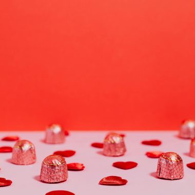Chocolates and heart decorations on a pink and red background, perfect for Valentine's.